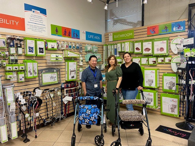 three staff members posing with rollator walkers inside of Atlantic Pharmacy & medical supplies, an independent shop, with NOVA medical products retail display on back wall