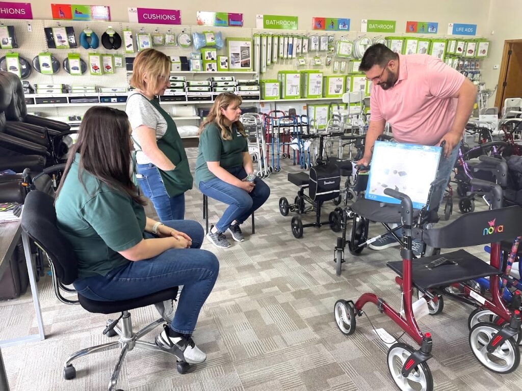 four staff members of Oswald’s Pharmacy reviewing NOVA home medical equipment details for better pharmacy marketing; NOVA product surrounds them on a showroom floor