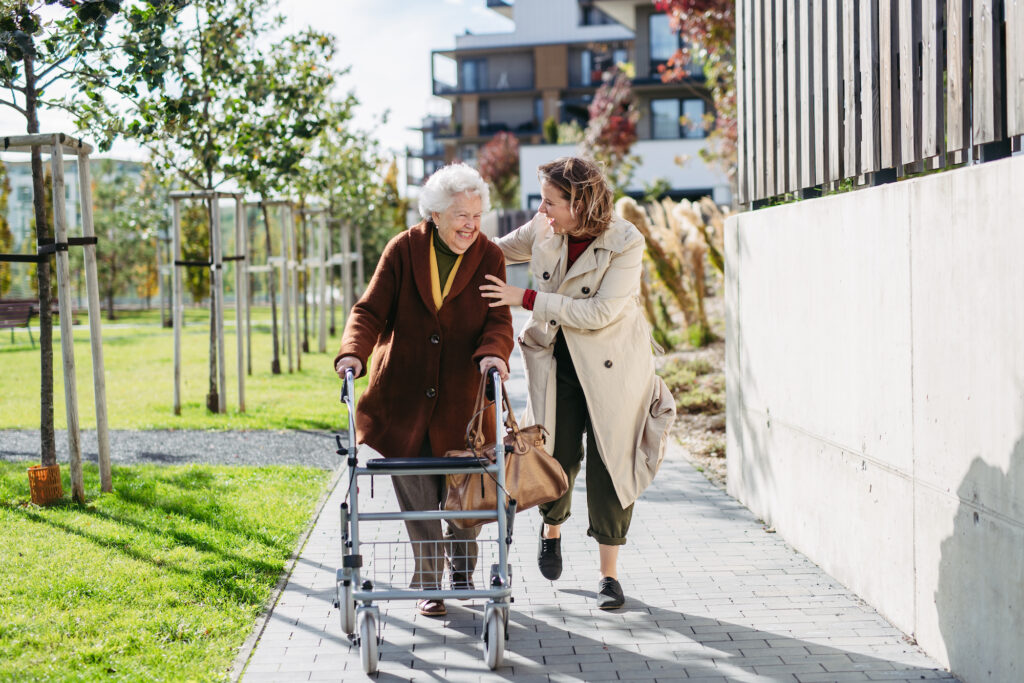 woman walking with another, older woman; outside as the older woman uses a rollator walker to prevent falls