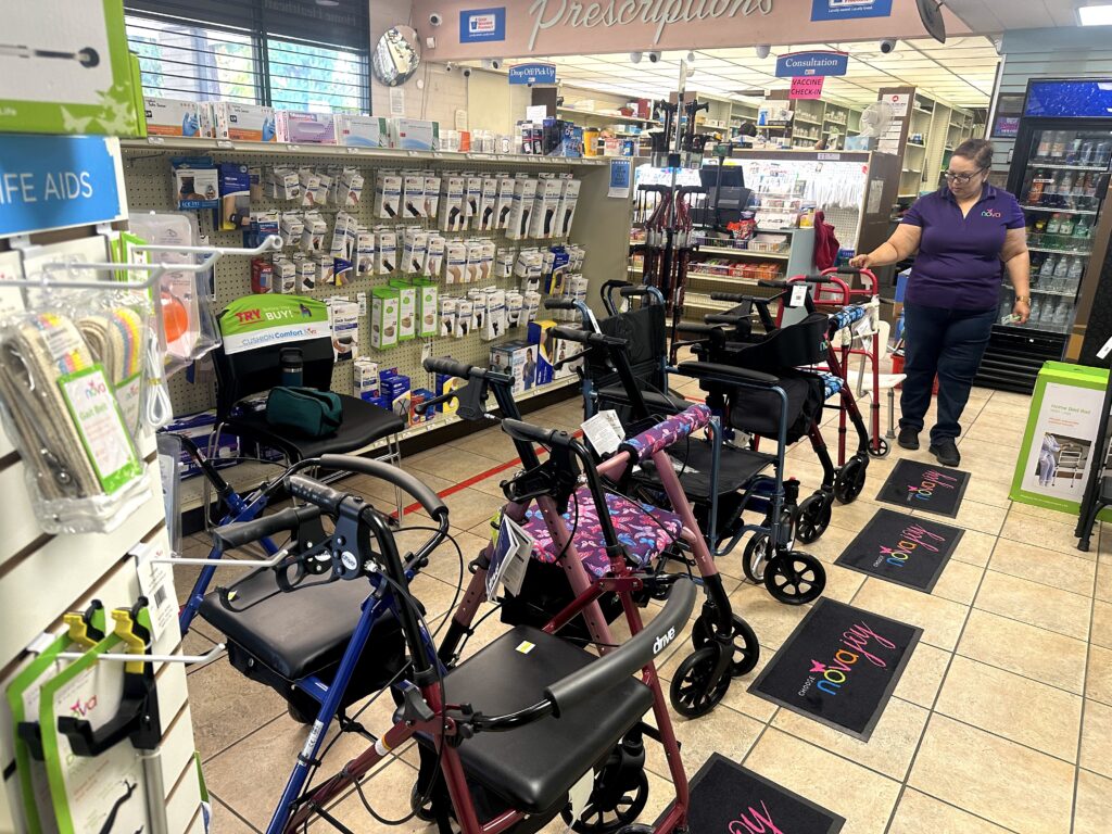 a NOVA sales representative inside Sierra Pharmacy, with a NOVA product wall display in the background and NOVA mobility walkers, rollators and transport chairs in the foreground