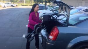 a woman easily lifts a rollator walker, folded, to place it into the trunk of a standard size sedan