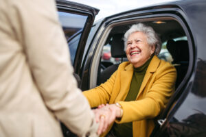someone helping an older woman out of the back seat of a vehicle, the woman is smiling as she accepts supportive hands