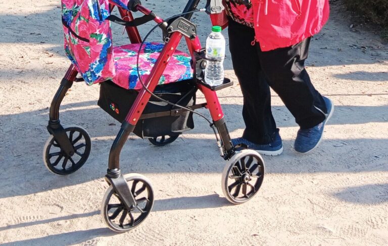 an older woman walks confidently with a NOVA rollator complete with mobility accessories, importance of cup holders on walkers