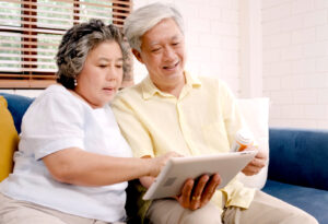 an older adult couple uses a tablet together with a prescription medication bottle handy, possibly engaged in a telehealth doctor appointment or consultation
